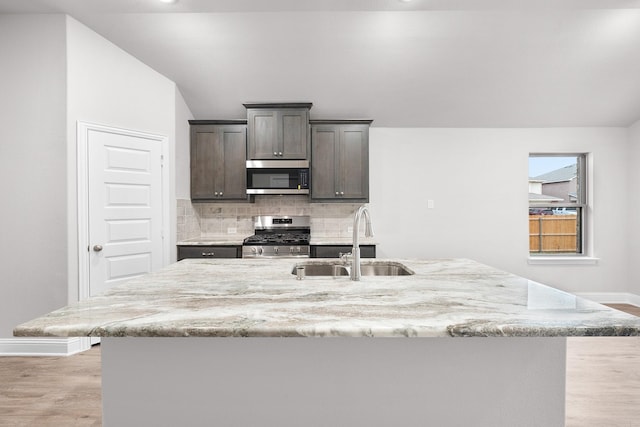 kitchen with baseboards, light wood finished floors, a sink, backsplash, and stainless steel appliances