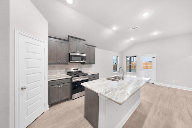 kitchen featuring appliances with stainless steel finishes, an island with sink, lofted ceiling, sink, and decorative backsplash