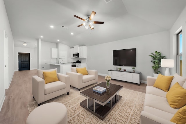 living room with light wood-type flooring, visible vents, baseboards, ceiling fan, and vaulted ceiling