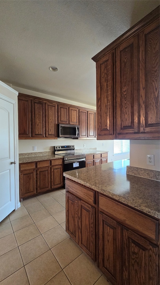 kitchen with a textured ceiling, stainless steel appliances, and light tile patterned floors