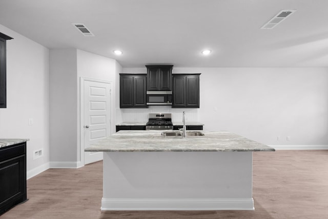 kitchen with sink, stainless steel appliances, light stone countertops, a center island with sink, and light wood-type flooring