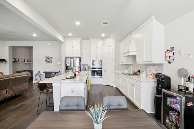 kitchen featuring light stone counters, an island with sink, stainless steel appliances, dark hardwood / wood-style floors, and a breakfast bar area