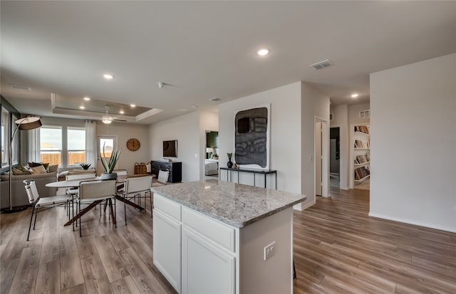 kitchen with white cabinets, light stone countertops, a tray ceiling, a center island, and light wood-type flooring