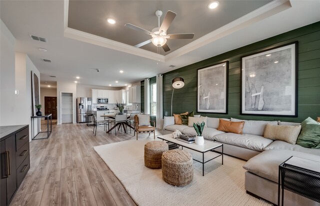 living room with a raised ceiling, light hardwood / wood-style flooring, and wooden walls