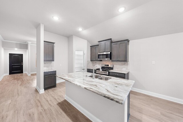 kitchen featuring sink, tasteful backsplash, a center island with sink, light wood-type flooring, and stainless steel appliances