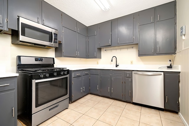 kitchen featuring light tile patterned flooring, gray cabinets, sink, appliances with stainless steel finishes, and a textured ceiling