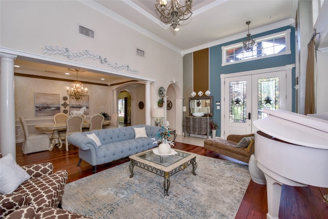 living room featuring ornamental molding, a chandelier, a high ceiling, ornate columns, and dark hardwood / wood-style flooring