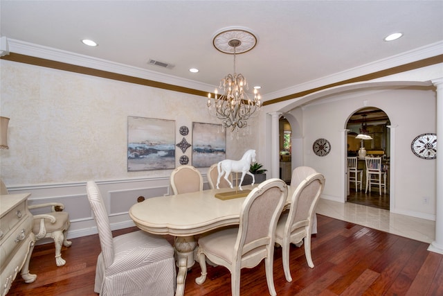 dining area featuring ornamental molding, a notable chandelier, decorative columns, and dark wood-type flooring