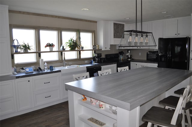 kitchen featuring dark wood-type flooring, sink, hanging light fixtures, white cabinets, and black appliances