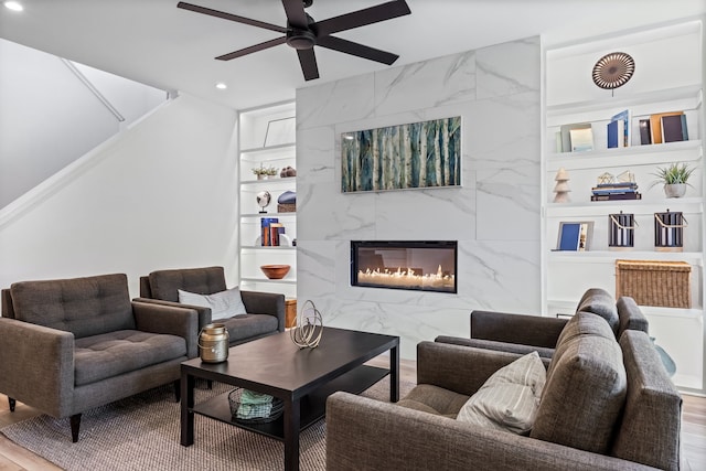 living room with a high end fireplace, hardwood / wood-style floors, built in shelves, and ceiling fan