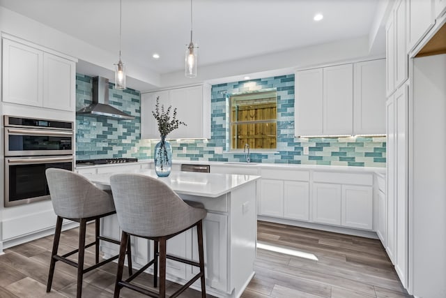 kitchen featuring tasteful backsplash, light hardwood / wood-style flooring, wall chimney exhaust hood, white cabinetry, and a center island