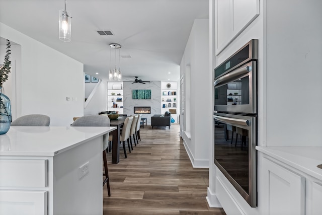 kitchen with a premium fireplace, stainless steel double oven, decorative light fixtures, and white cabinets