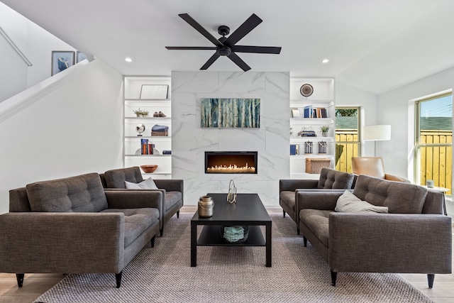 living room featuring ceiling fan, lofted ceiling, a premium fireplace, and built in shelves