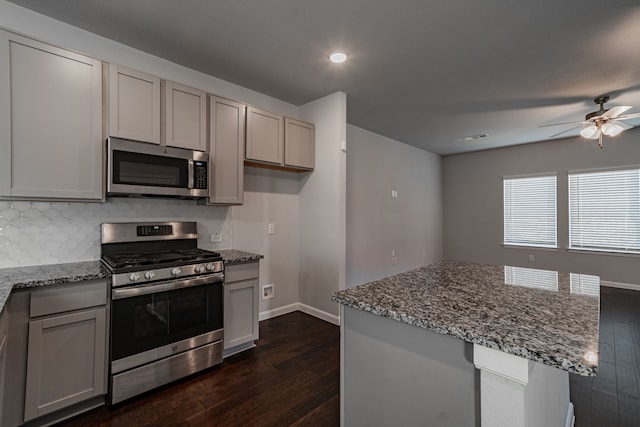 kitchen featuring gray cabinetry, backsplash, ceiling fan, light stone countertops, and appliances with stainless steel finishes