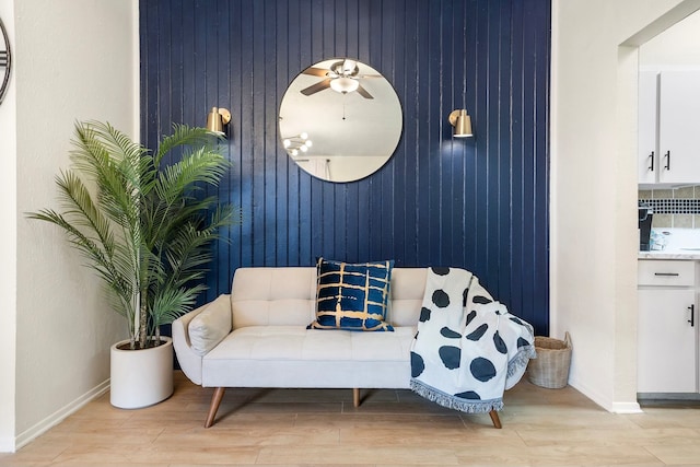 living area featuring light wood-type flooring, wood walls, and ceiling fan