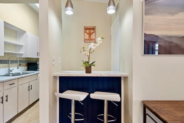 kitchen featuring light hardwood / wood-style floors, white cabinetry, sink, tasteful backsplash, and pendant lighting