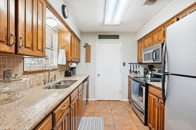 kitchen featuring light stone countertops, stainless steel appliances, sink, light tile patterned floors, and backsplash