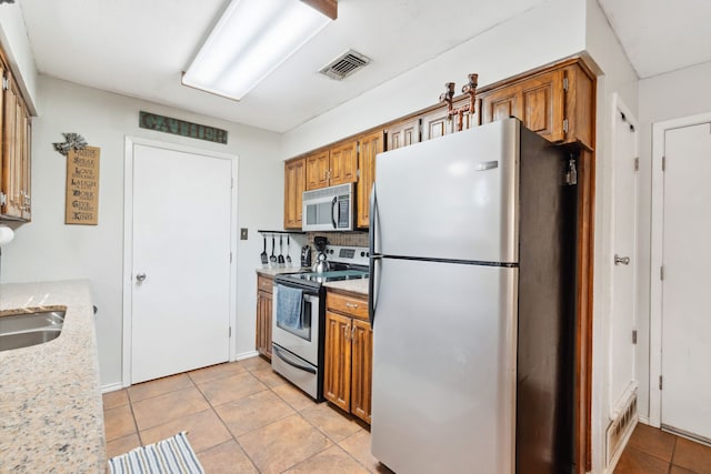 kitchen featuring appliances with stainless steel finishes, light stone countertops, light tile patterned floors, and tasteful backsplash