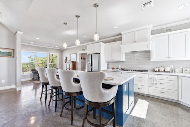 kitchen featuring an island with sink, white cabinetry, appliances with stainless steel finishes, decorative light fixtures, and a kitchen breakfast bar