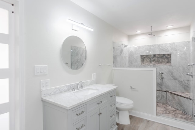 bathroom featuring hardwood / wood-style flooring, vanity, tiled shower, and toilet