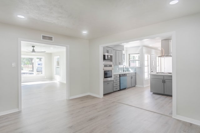 kitchen with stainless steel appliances, wall chimney range hood, and light wood-type flooring