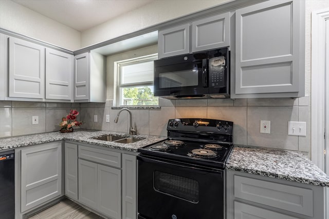 kitchen featuring black appliances, light stone countertops, decorative backsplash, sink, and gray cabinets