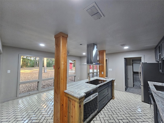 kitchen with ornate columns, island exhaust hood, light stone counters, appliances with stainless steel finishes, and a textured ceiling