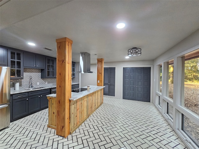 kitchen featuring stainless steel fridge, sink, wall chimney range hood, black stovetop, and decorative backsplash