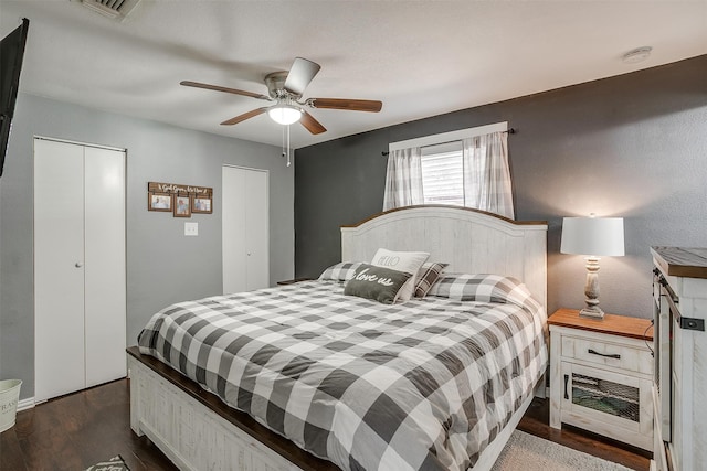 bedroom featuring ceiling fan, dark hardwood / wood-style floors, and two closets