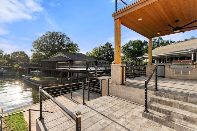 view of patio with a water view, ceiling fan, area for grilling, and exterior kitchen