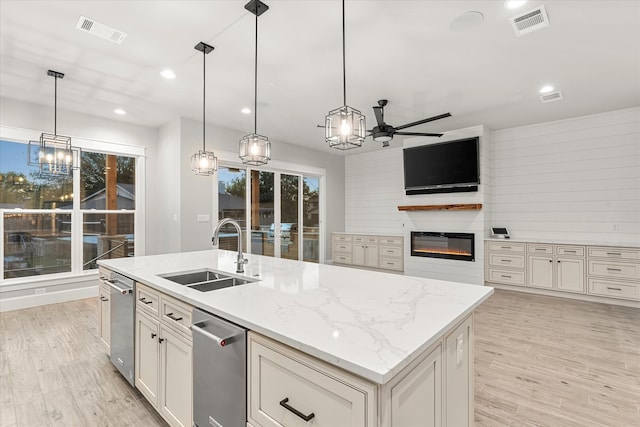 kitchen featuring light wood-type flooring, pendant lighting, a center island with sink, sink, and light stone countertops