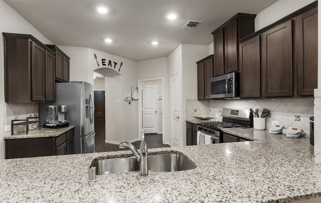 kitchen with tasteful backsplash, dark brown cabinets, sink, light stone countertops, and appliances with stainless steel finishes