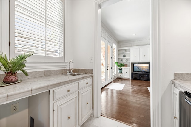 kitchen with light wood-type flooring, sink, tile countertops, and white cabinets