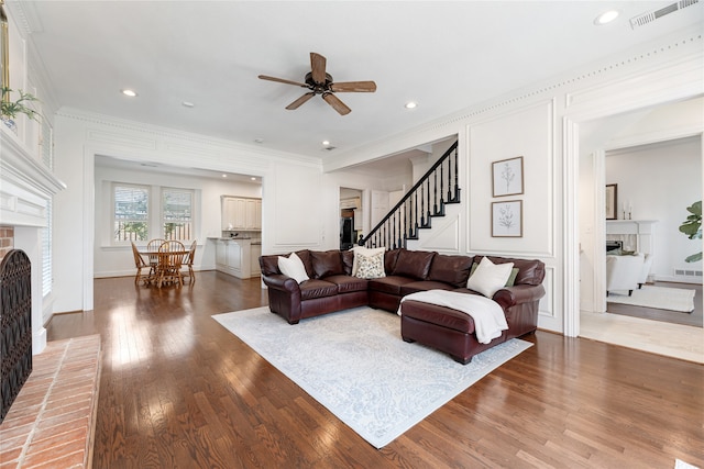 living room with a brick fireplace, crown molding, hardwood / wood-style floors, and ceiling fan