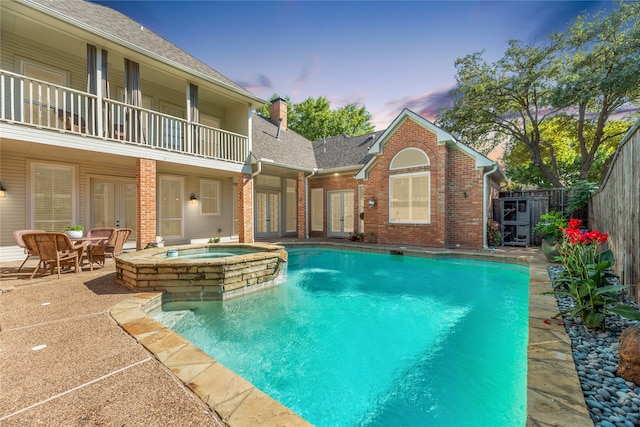 pool at dusk featuring an in ground hot tub and a patio