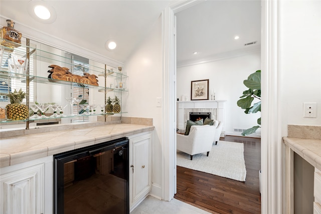 bar featuring light wood-type flooring, a brick fireplace, white cabinetry, wine cooler, and tile countertops