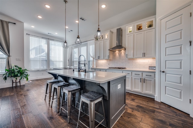 kitchen with wall chimney exhaust hood, white cabinets, a center island with sink, and sink