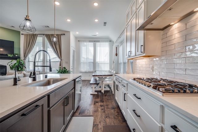 kitchen featuring dark wood-type flooring, sink, extractor fan, pendant lighting, and appliances with stainless steel finishes