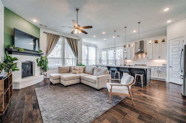 living room featuring a brick fireplace, dark hardwood / wood-style floors, sink, and ceiling fan