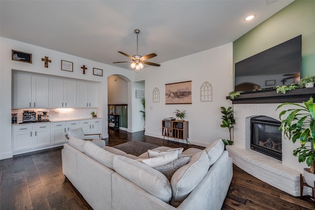 living room featuring a brick fireplace, dark hardwood / wood-style floors, and ceiling fan