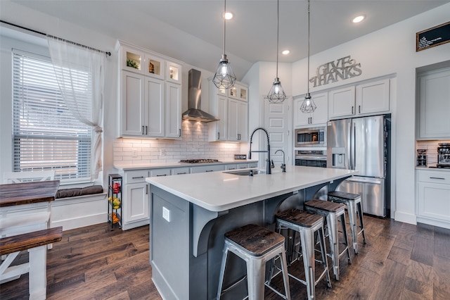 kitchen featuring dark hardwood / wood-style floors, wall chimney exhaust hood, sink, appliances with stainless steel finishes, and a center island with sink