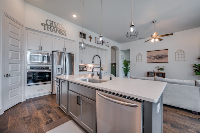 kitchen featuring dark wood-type flooring, decorative light fixtures, sink, stainless steel appliances, and an island with sink