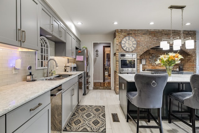 kitchen with stainless steel appliances, sink, hanging light fixtures, a breakfast bar area, and gray cabinets