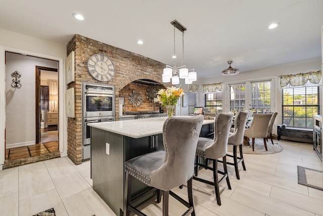 kitchen featuring a kitchen island, a breakfast bar, stainless steel double oven, a notable chandelier, and hanging light fixtures