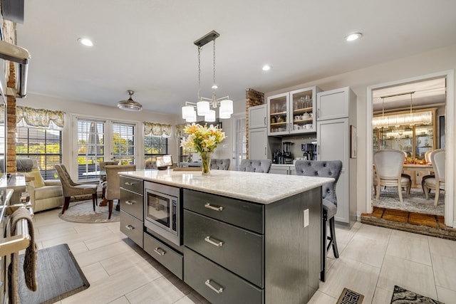 kitchen with a center island, white cabinets, stainless steel microwave, a kitchen bar, and decorative light fixtures