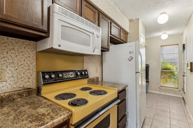 kitchen with light tile patterned floors, a textured ceiling, and white appliances