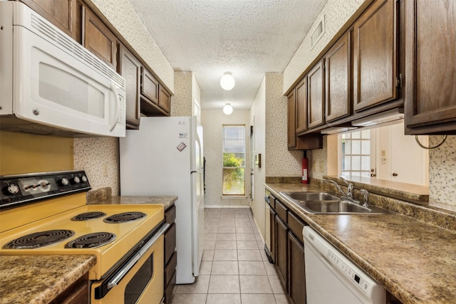 kitchen featuring sink, white appliances, light tile patterned floors, and a textured ceiling