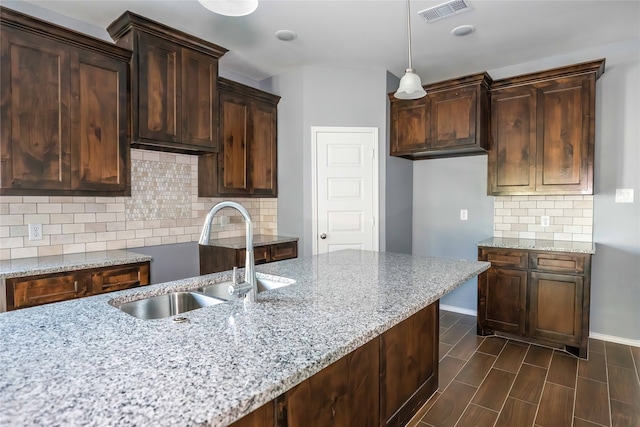 kitchen with pendant lighting, light stone counters, sink, and tasteful backsplash