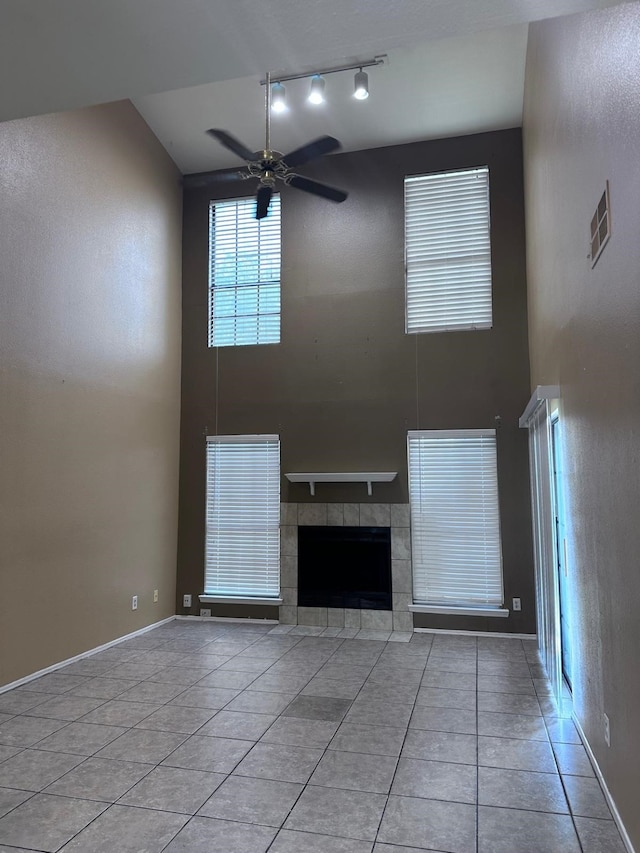 unfurnished living room featuring a tile fireplace, ceiling fan, a towering ceiling, and light tile patterned floors