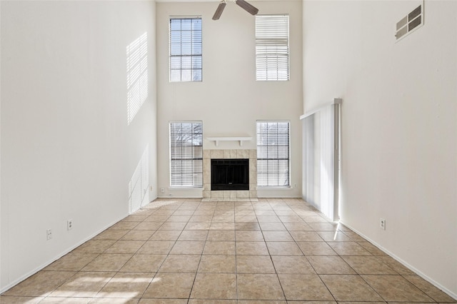 unfurnished living room with a wealth of natural light, ceiling fan, a tiled fireplace, and light tile patterned floors